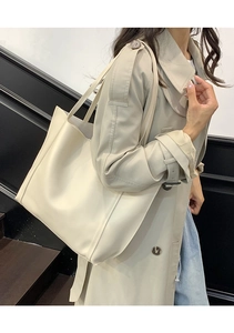 Detail of a large cream tote bag with elegant stitching shown against a trench coat