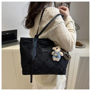 Dettaglio della borsa tote nera plissettata con ciondolo a forma di orsetto blu