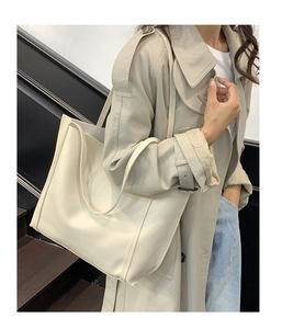 Dettaglio di una grande borsa tote minimalista color crema abbinata a un trench