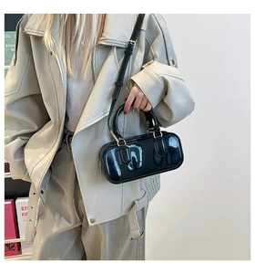 Detail view of stylish black glossy PVC crossbody bag with gold hardware on a model
