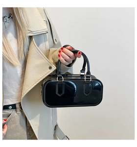 Detail of glossy black patent leather pillow bag with gold metal hardware on cream jacket