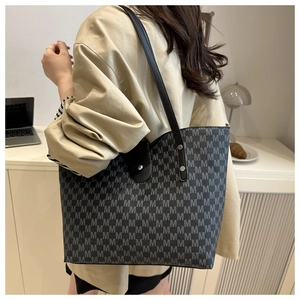 Detail of large tote bag with M-letter print and black leather strap on a model shoulder