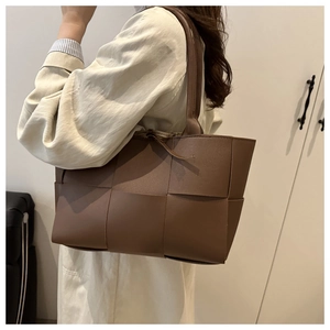 Side view of brown wide-woven leather tote bag worn as an underarm shoulder bag