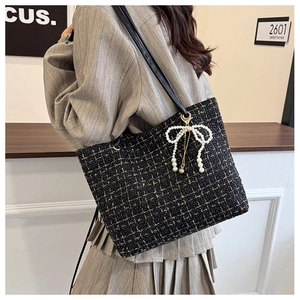 Detail der schwarz-goldenen Tweed-Tasche mit dekorativem Anhänger aus weißen Perlen