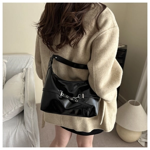 Detail of black glossy leather dumpling bag with metal eyelets and adjustable buckle strap