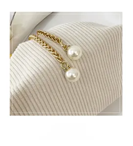 Dettaglio di catena dorata con perle bianche e cristalli su tessuto a maglia beige