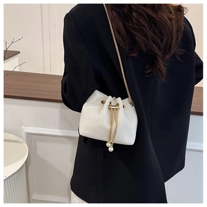 Dettaglio di una borsa a secchiello bianca a pieghe con catena dorata e perle su una modella