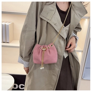 Borsa a secchiello rosa con catena dorata e perle indossata con un trench beige dal look moderno