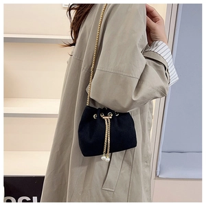 Dettaglio borsa a secchiello in velluto nero con catena dorata e elegante ciondolo perla
