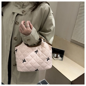 Detailed view of quilted pink handbag with embroidered bows and leather handles