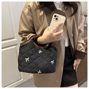 Detail of black quilted handbag with white 3D bows and contrast brown leather handles
