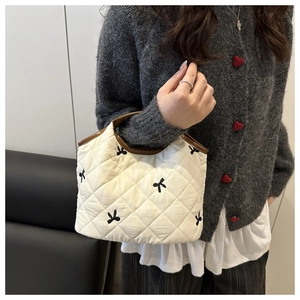 Detail of white quilted handbag with black bow embroidery and brown trim edges