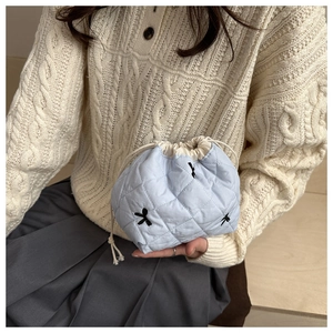 Close-up of light blue quilted drawstring bag with delicate black bow embroidery detail