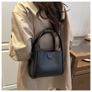 Minimalist black leather crossbody bag with dual handles shown on a model in a warm interior
