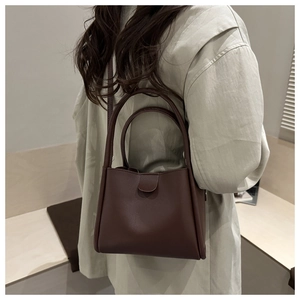 Detail of dark coffee bucket bag showing premium leather texture and dual handle design