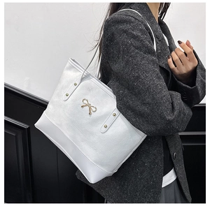 Détail du sac cabas blanc avec fermoir nœud doré sur un modèle en manteau de laine