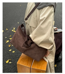 Outdoor shot of a brown matte tote bag with adjustable strap on a beige trench coat