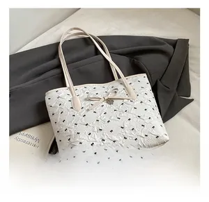 Détail du sac cabas matelassé blanc avec motifs de nœuds noirs et pendentif en cœur