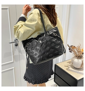 Detail of black glossy tote bag with embossed bow patterns and adjustable side buckle