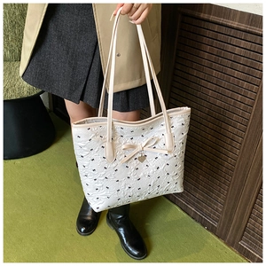 Détail du sac cabas matelassé blanc avec motifs de nœuds noirs et pendentif cœur