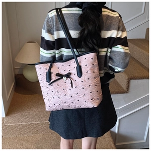 Grand sac cabas rose avec imprimés nœuds et pendentif cœur porté par un mannequin