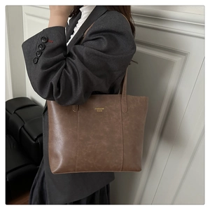 Detailed view of brown leather tote bag with gold lettering held by a model in a suit
