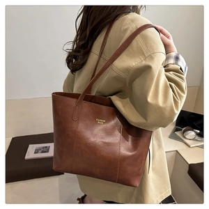 Détail de la texture du cabas en cuir marron et du logo doré sur le côté du sac