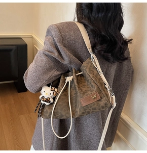 Detail of leopard print bucket bag with drawstring closure and plush character pendant