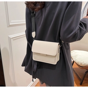 Detail of cream crossbody square bag with wide black strap shown on model shoulder
