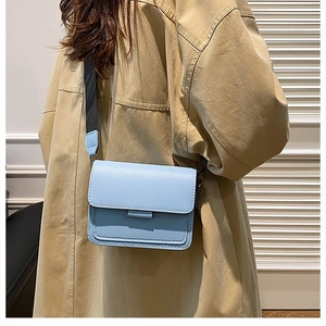 Back side view of light blue square crossbody bag with wide strap on beige coat model