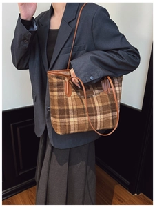 Detail of a brown plaid tote bag with leather handles shown on a model in a gray suit