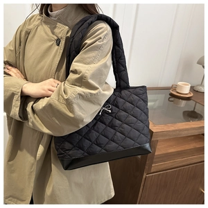 Close-up of a black quilted tote bag with a silver metal bow and thick padded shoulder straps