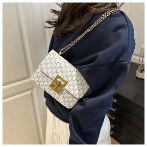 Detailed view of white crossbody bag with grey M pattern and gold chain on model