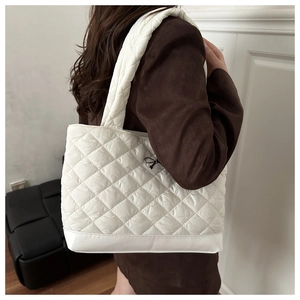 Close-up of white quilted tote bag with silver bow charm and wide shoulder strap