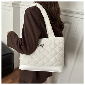 Detail of white quilted tote bag featuring a delicate black bow and stitched pattern