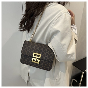Detail of a brown leather crossbody bag with M-pattern and gold chain strap worn by model