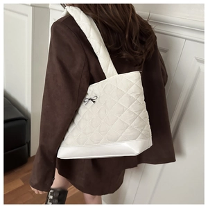 Detailed view of white quilted shoulder tote bag with a black bow and classic diamond pattern