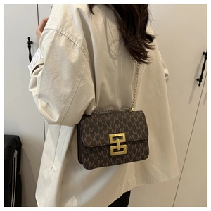 Detail of a brown crossbody bag with M-pattern and gold chain strap on a model