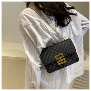 Detail of black monogram shoulder bag with gold chain strap worn by a model