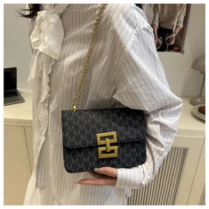 Detail of black crossbody bag with gold M-pattern print and metallic chain strap