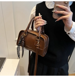 Detail of dark brown leather Boston bag with woven pendant and adjustable strap