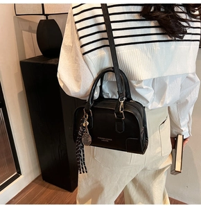 Detail of black leather bowling bag featuring metal tennis racket charm and tassel
