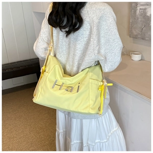 Detail of light yellow nylon bag featuring adjustable wide shoulder strap and side drawstrings