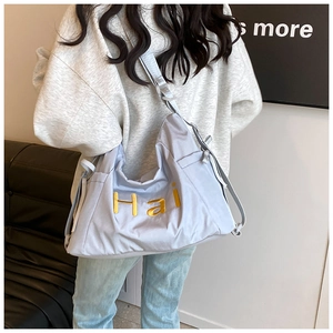 Macro detail of a light blue nylon tote bag featuring yellow Hai letter embroidery