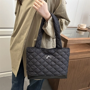 Black quilted tote bag with silver bow detail and glossy base shown on a model