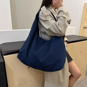 Große dunkelblaue Hobo-Tasche aus wasserdichtem Nylon, getragen zu einem Trenchcoat