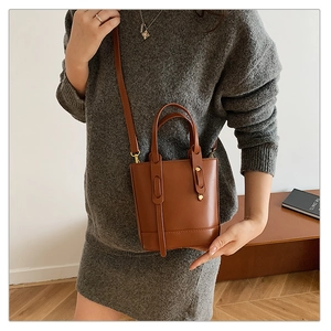 Brown leather bucket bag with top handle and adjustable strap in a cozy home setting