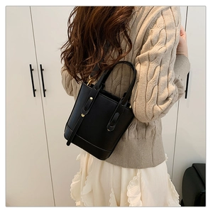 Detail of a black leather bucket bag with gold rivets and adjustable shoulder strap