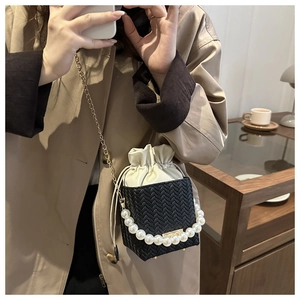 Detail of mini black woven bucket bag with pearl handle and gold chain strap