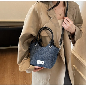 Dettaglio della borsa a spalla in denim con manici in pelle nera e finiture metalliche